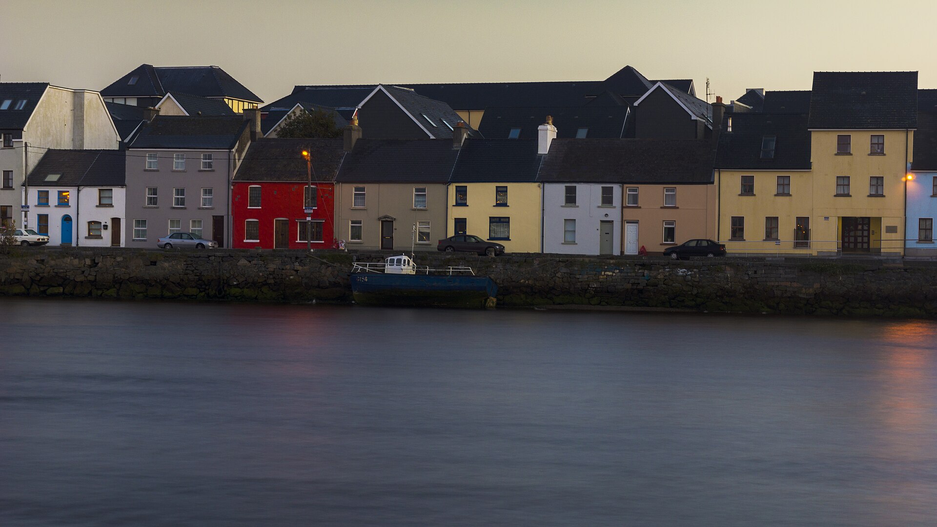 A boat and the colourful Long Walk waterfront at sunrise, viewed across the River Corrib from the Claddagh in Galway.